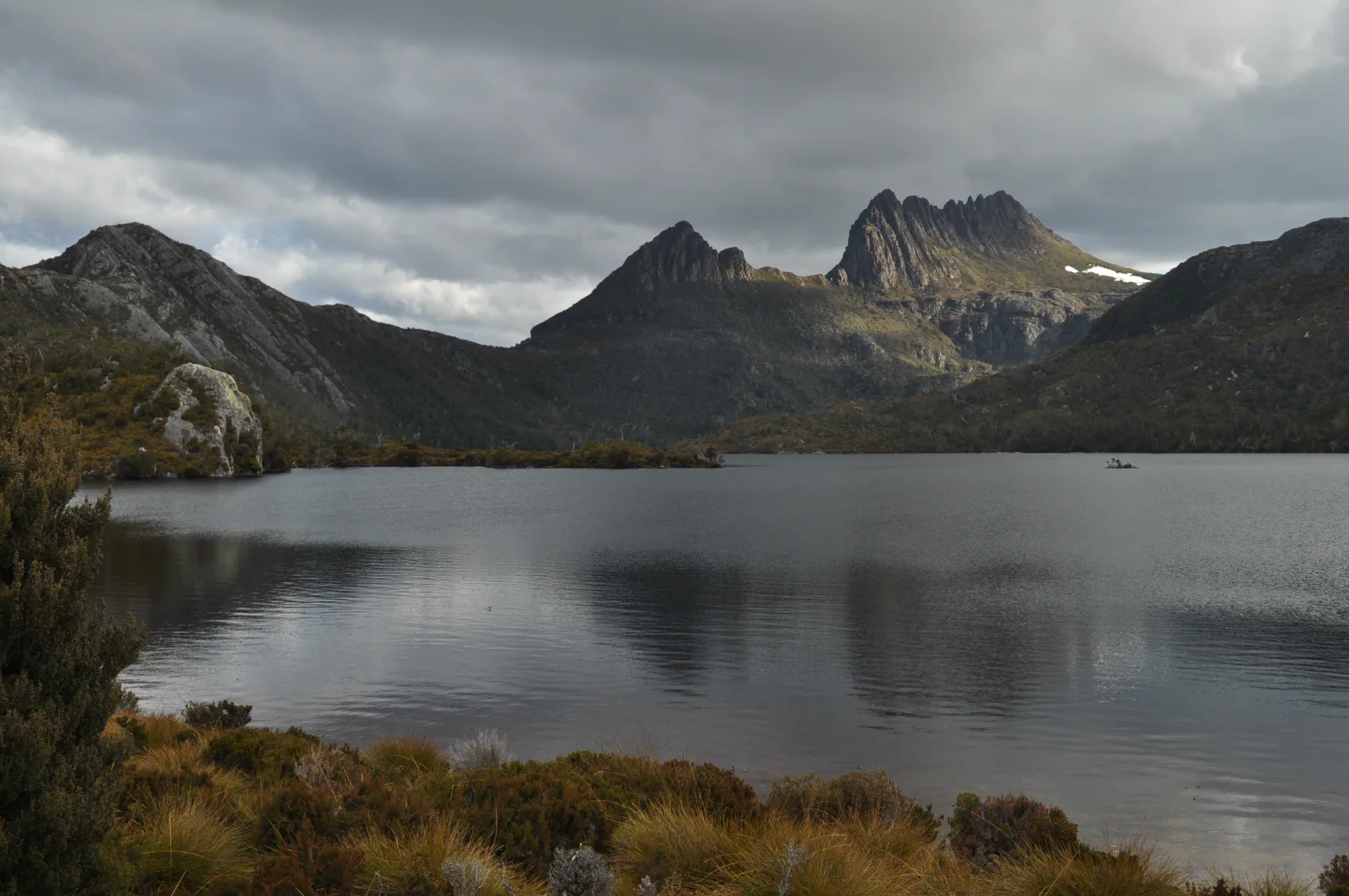 Cradle Mountain beneath heavy clouds above the still waters of Dove Lake in Tasmania, Australia