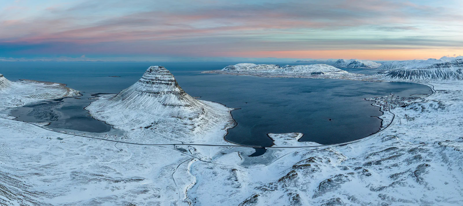 Kirkjufell in a snowy winter panorama, with the bay and distant mountains under soft morning light